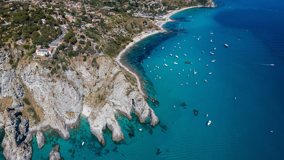 A coastal town with rocky cliffs, clear turquoise waters, and numerous boats.