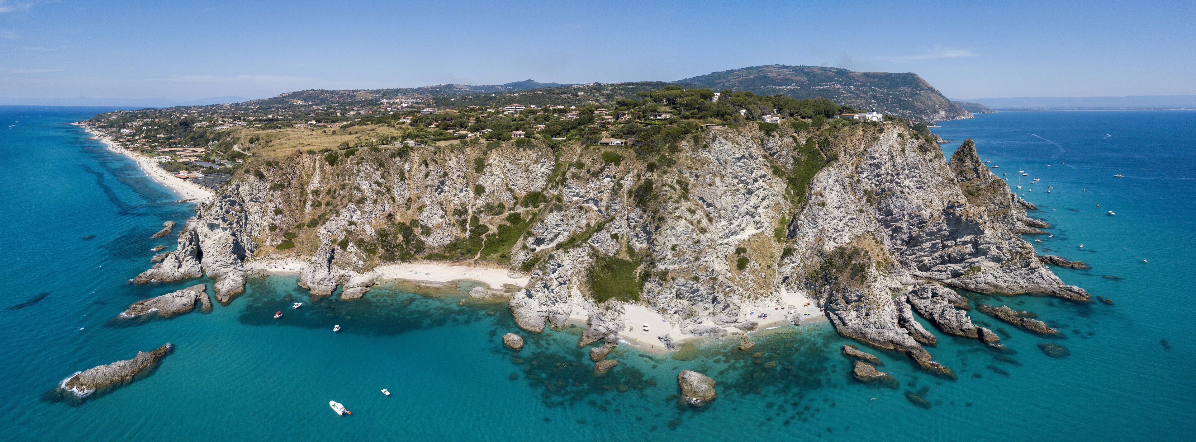 A coastal landscape with a rocky peninsula, clear turquoise waters, and a distant town.