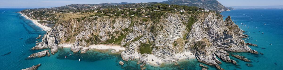 A coastal landscape with a rocky peninsula, clear turquoise waters, and a distant town.
