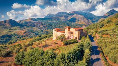 A historic building with red-tiled roofs, surrounded by lush green hills and mountains.