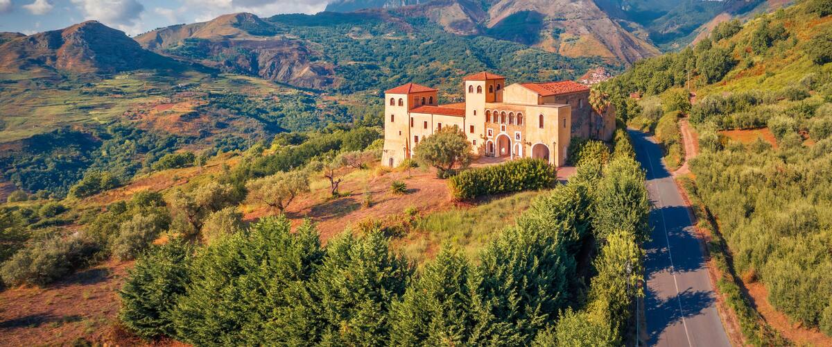 A historic building with red-tiled roofs, surrounded by lush green hills and mountains.