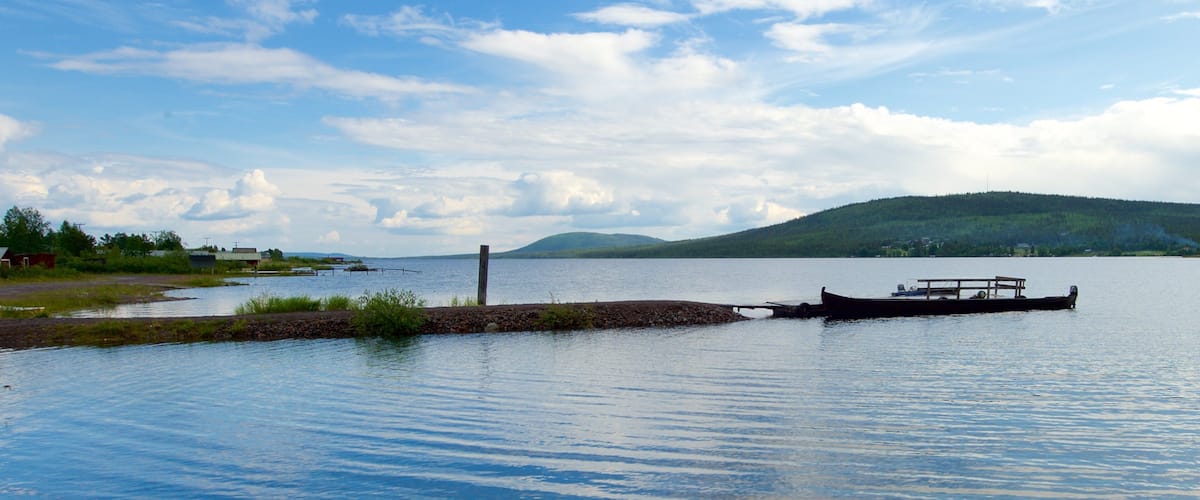 A calm lake with a wooden dock extending into the water, surrounded by greenery and distant hills.