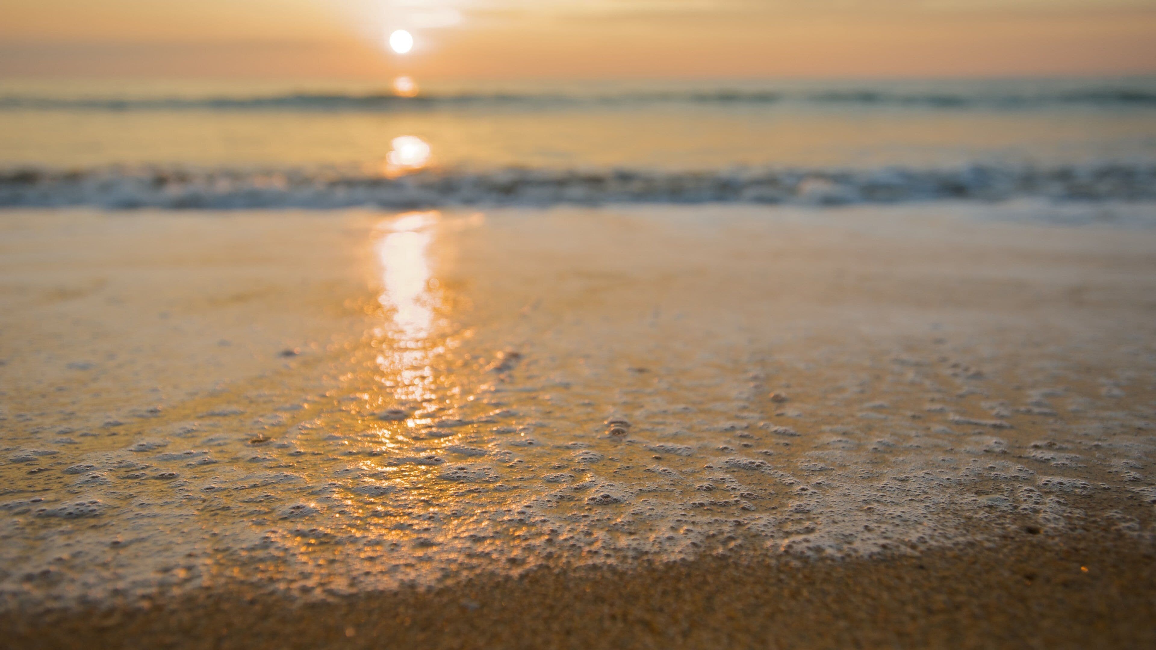 Uma praia ao pôr do sol, com o sol refletindo na areia molhada.