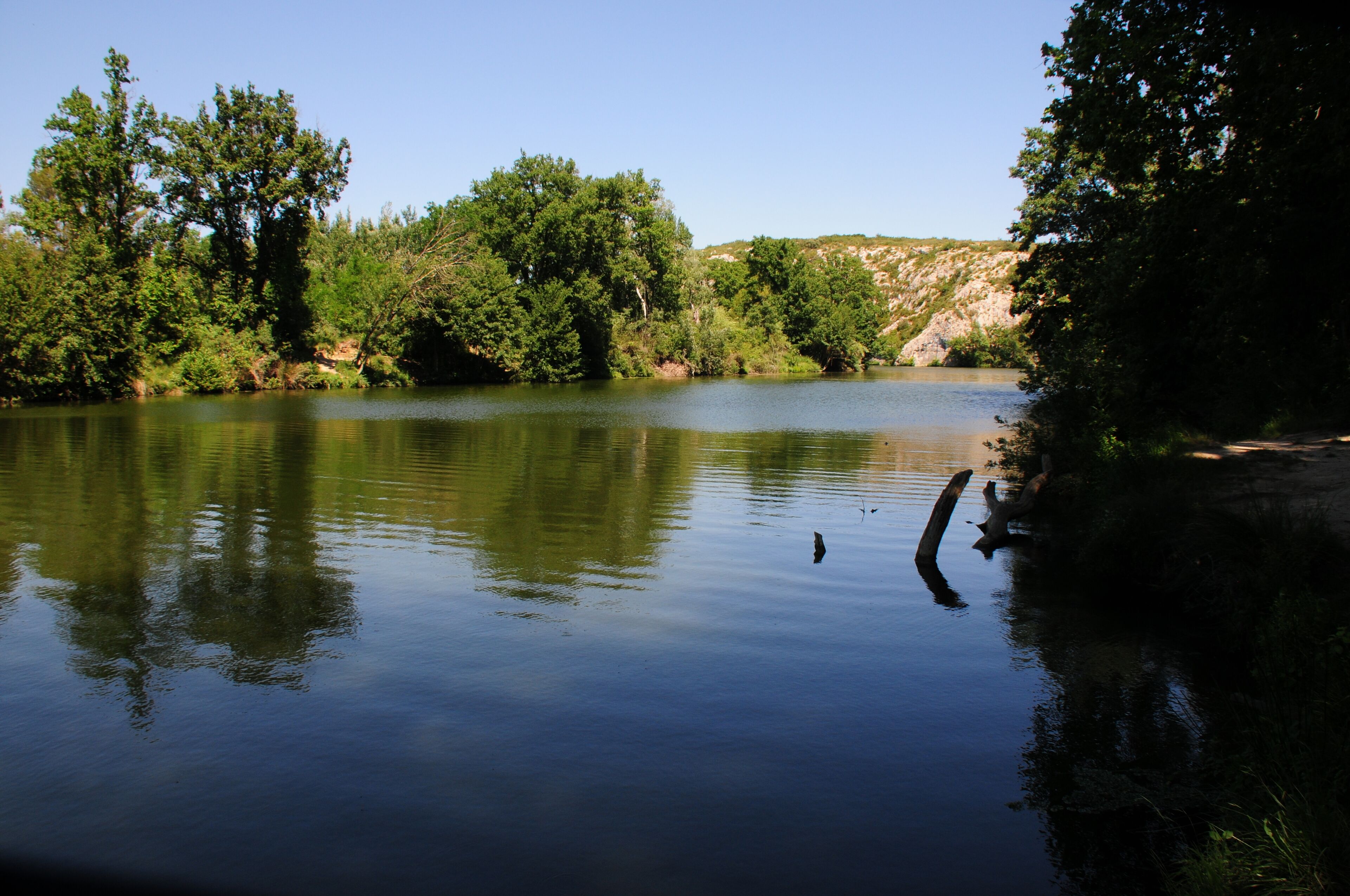 A calm river surrounded by dense trees and a rocky hillside.