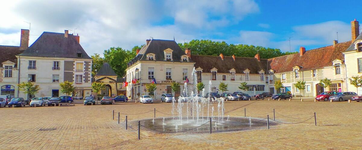 A cobblestone square with a central fountain, surrounded by historic buildings with European architecture.