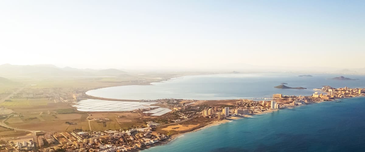 An aerial view of a coastal city with a long beachfront, dense urban area, and a large body of water.