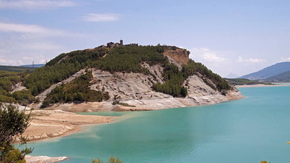 Un paysage côtier avec une colline recouverte de végétation et une mer turquoise aux eaux limpides.