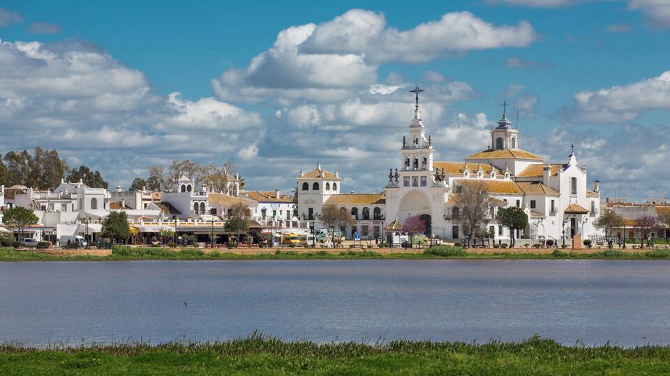 A white church with a bell tower and a large dome, surrounded by a body of water and greenery.