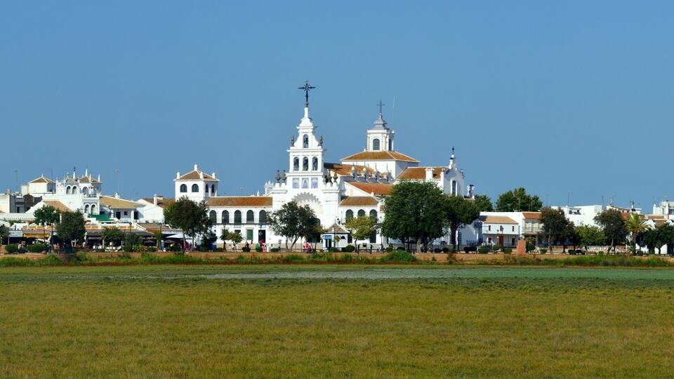 A coastal town with white buildings, a prominent church with a tall bell tower, and a clear blue sky.