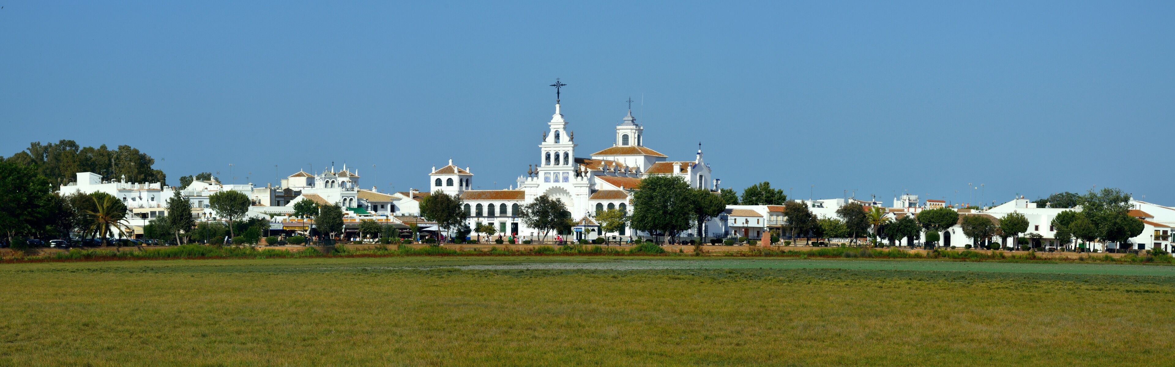 A coastal town with white buildings, a prominent church with a tall bell tower, and a clear blue sky.