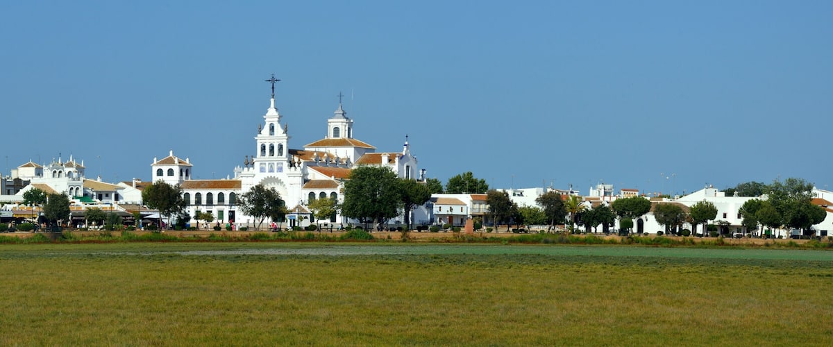 A coastal town with white buildings, a prominent church with a tall bell tower, and a clear blue sky.