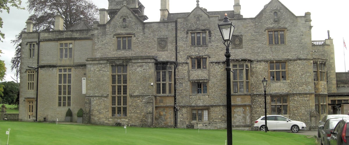 A historic stone building with multiple chimneys and a well-maintained lawn in front.