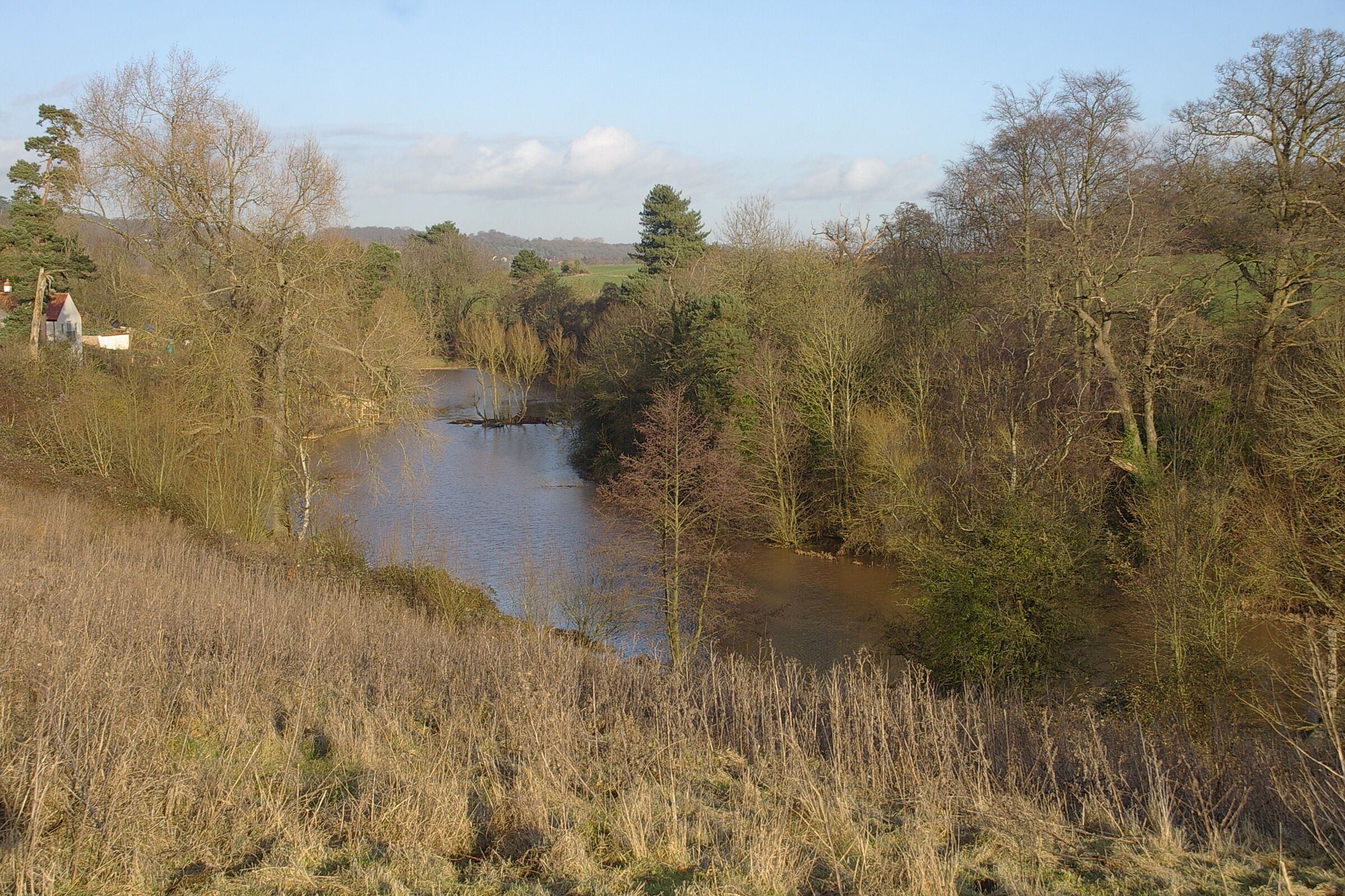 A river flowing through a wooded area with a small house on the left bank.