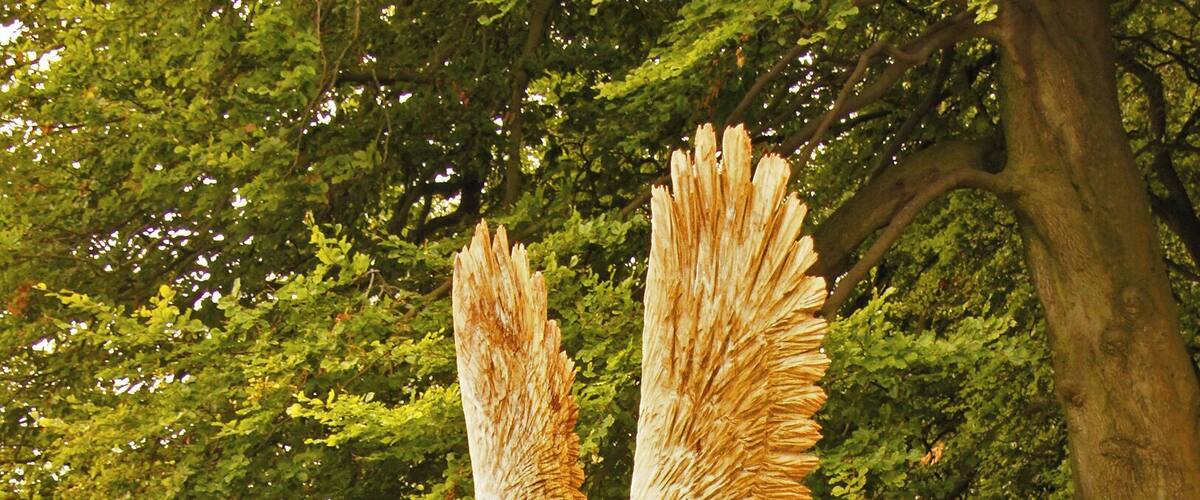 A wooden sculpture of an eagle perched on a tree stump in a forest.