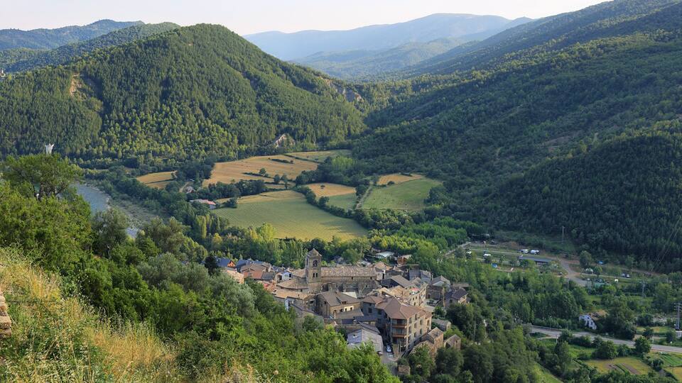 A valley with a river, surrounded by hills and a small town with historic buildings.