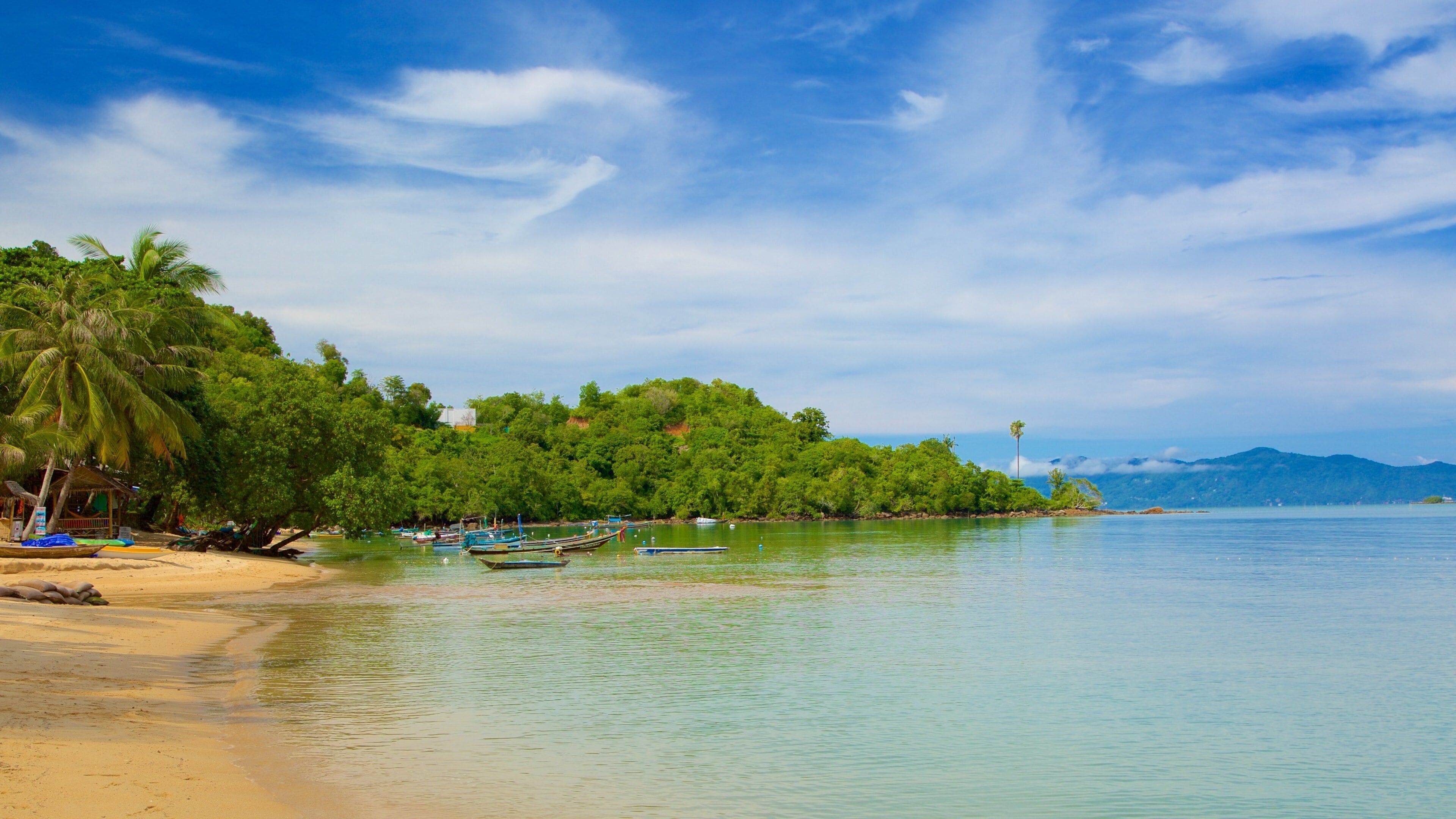 A tropical beach with clear waters, boats, and lush greenery.