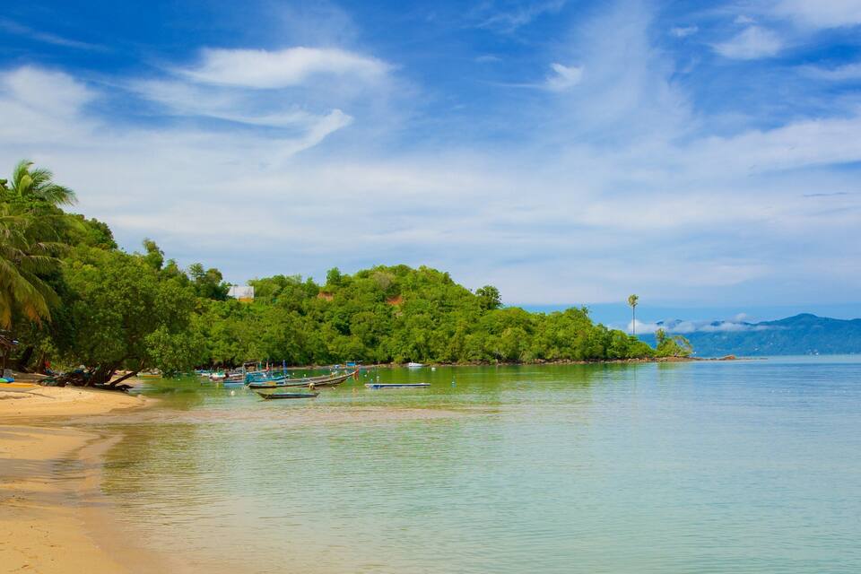 Una playa tropical con aguas cristalinas, embarcaciones y exuberante vegetación.