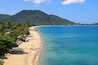 A tropical beach with clear turquoise waters, a sandy shore, and a lush green mountain in the background.