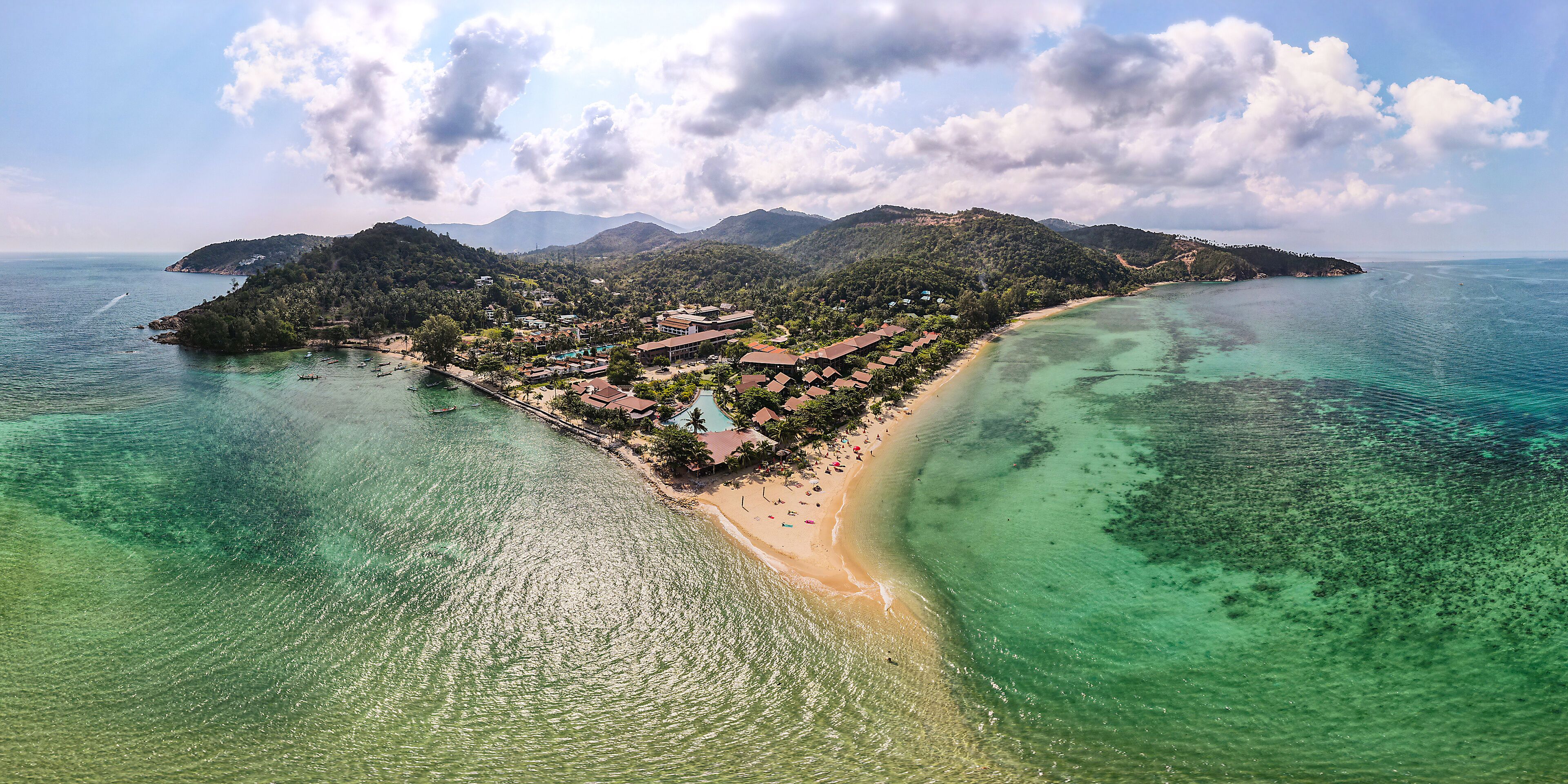 A coastal resort with a beach, clear turquoise waters, and lush green hills in the background.