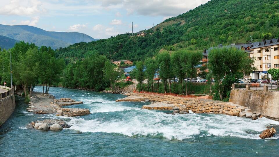 A river with a rocky bed, surrounded by lush greenery and a hillside.