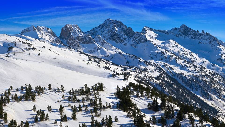 A snow-covered mountain range with a ski resort and a clear blue sky.
