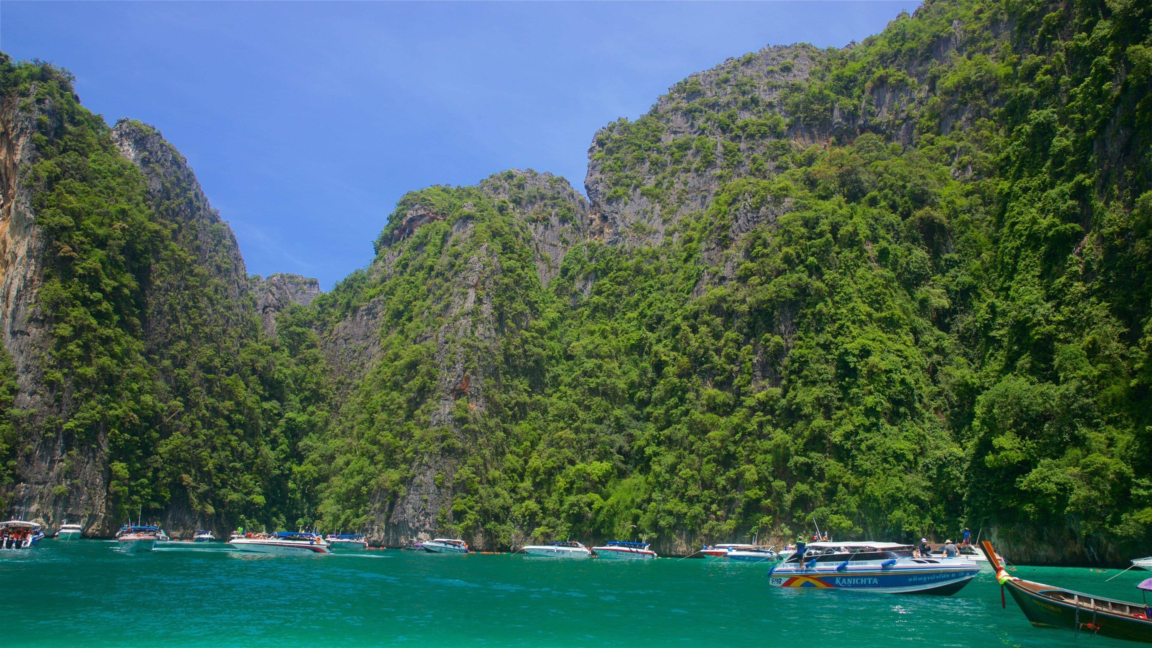 A coastal scene with boats on turquoise water, surrounded by lush green cliffs.
