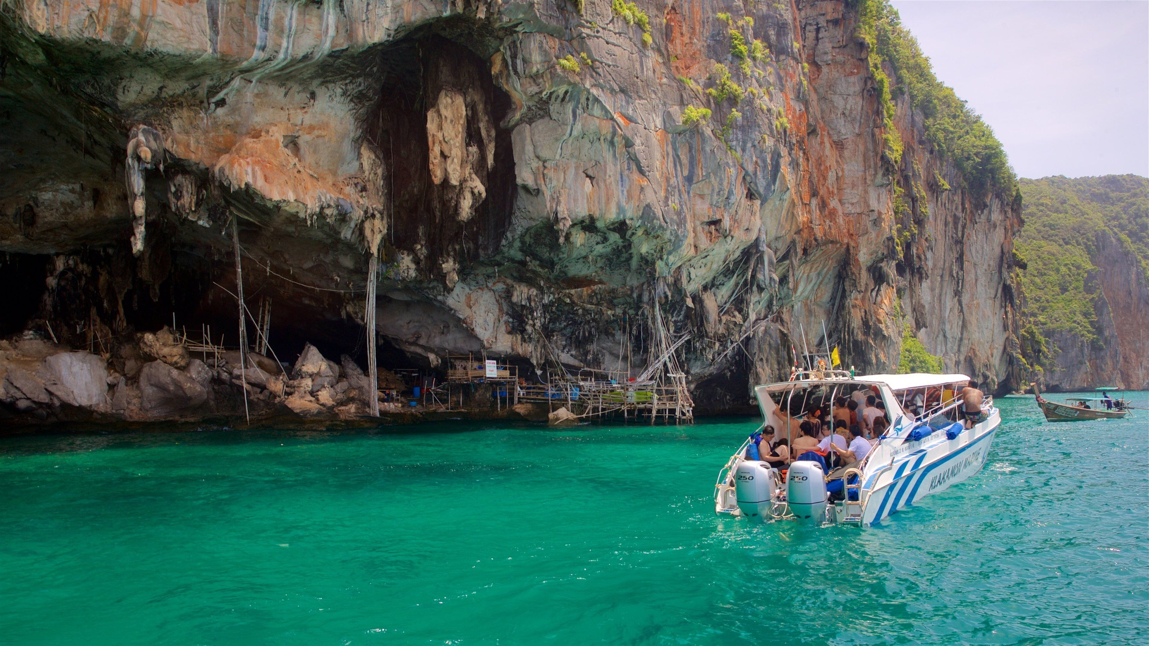 A boat with passengers near a rocky cliff and clear turquoise water.