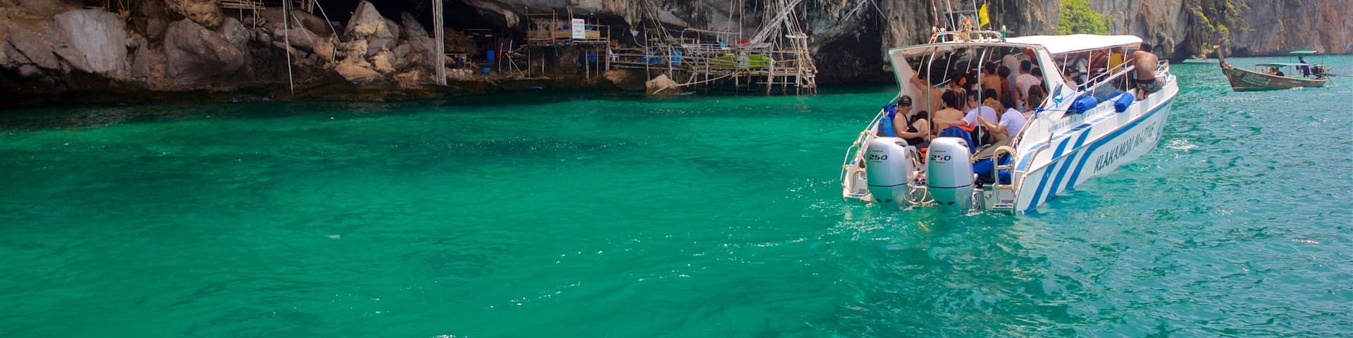 A boat with passengers near a rocky cliff and clear turquoise water.