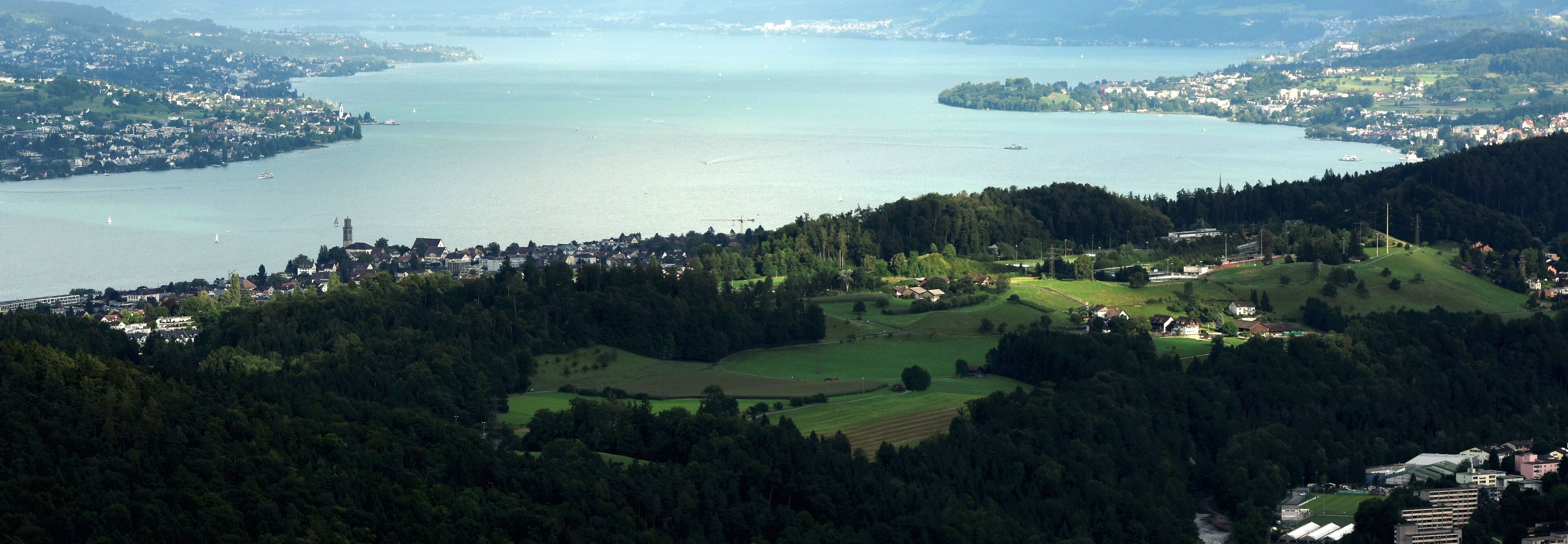 A panoramic view of a lake surrounded by hills and a town.