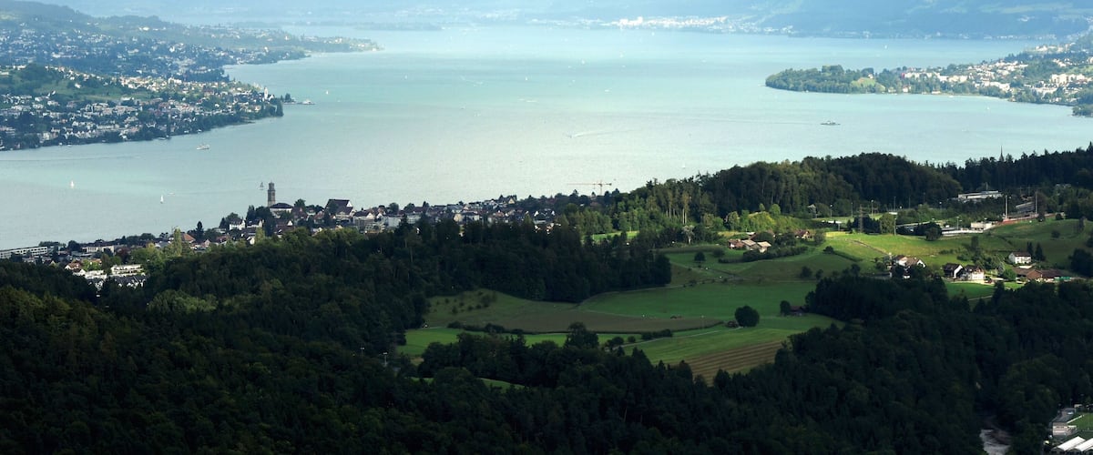 A panoramic view of a lake surrounded by hills and a town.