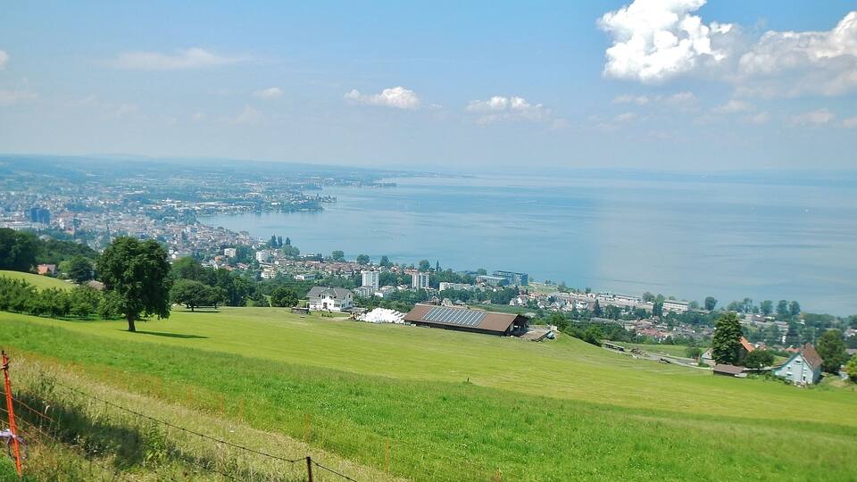A coastal cityscape with a large body of water, green fields, and residential buildings.