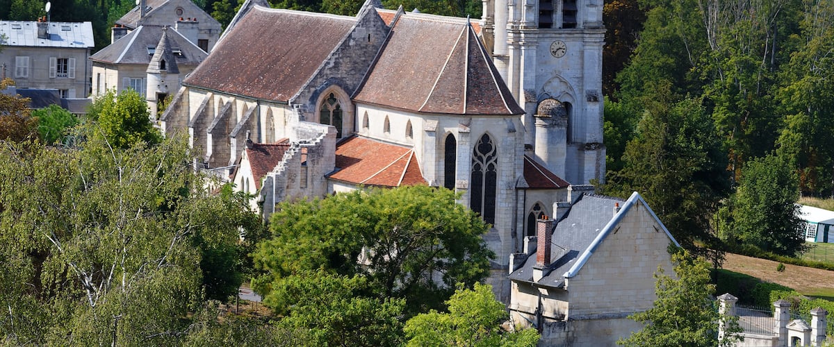 A historic church with a bell tower, surrounded by lush greenery and other buildings.