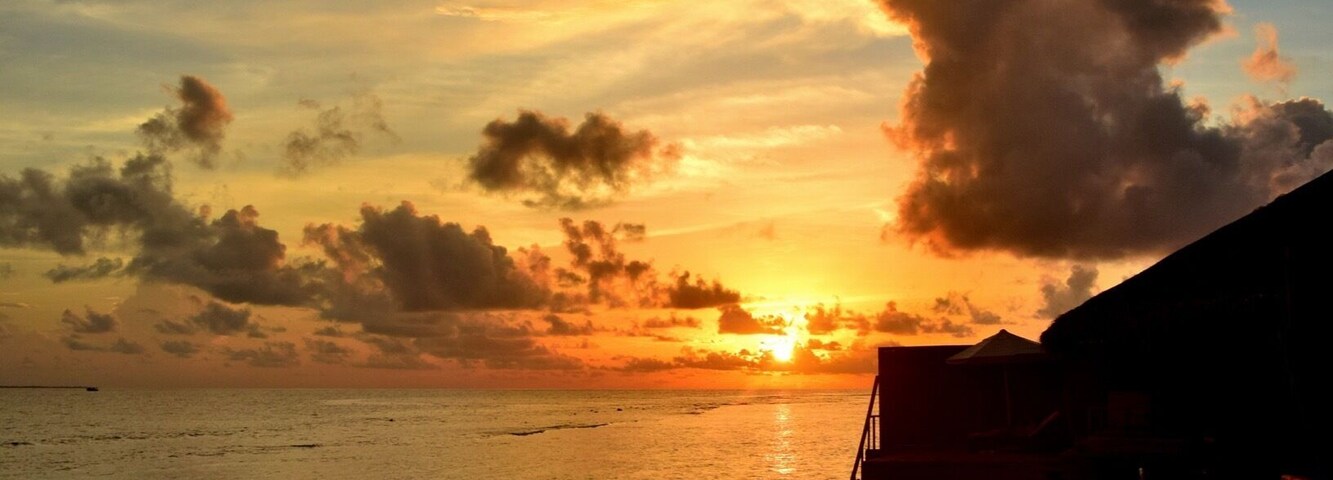 Atardecer sobre un mar tranquilo con un muelle de madera y un edificio pequeño.