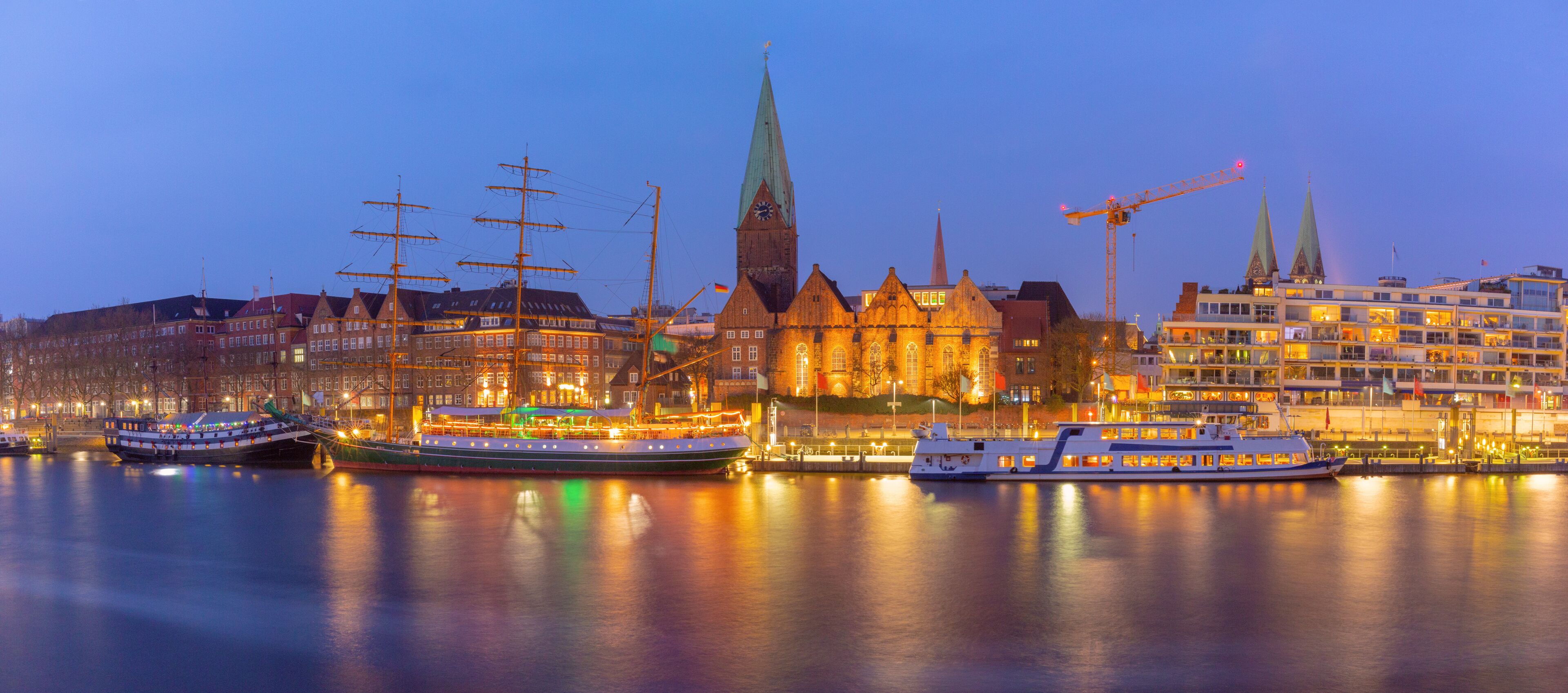 A cityscape with a prominent church, several boats docked at the waterfront, and modern buildings in the background.