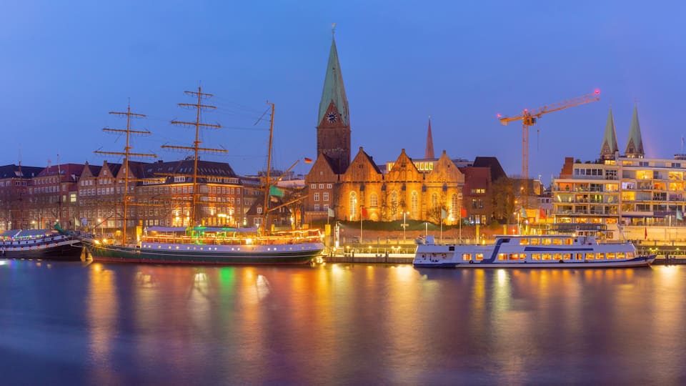 A cityscape with a prominent church, several boats docked at the waterfront, and modern buildings in the background.