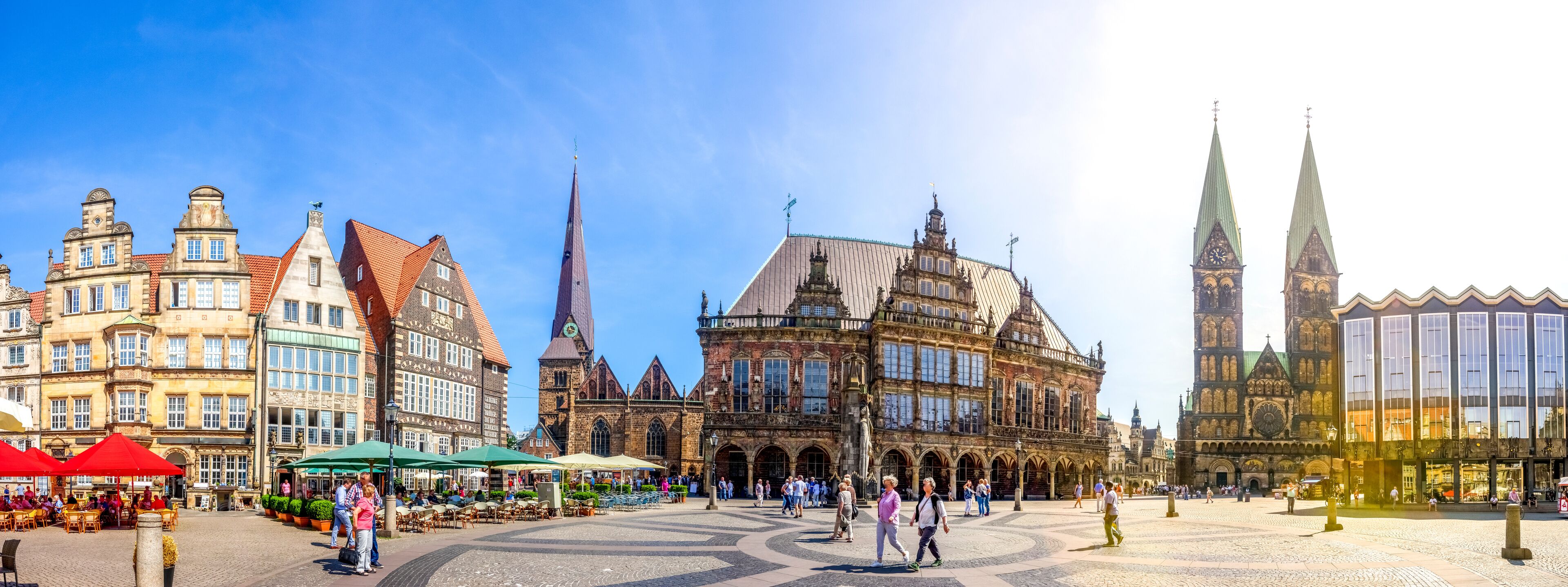 A historic square with cobblestone pavement, a prominent church with a tall spire, and a mix of traditional and modern buildings.