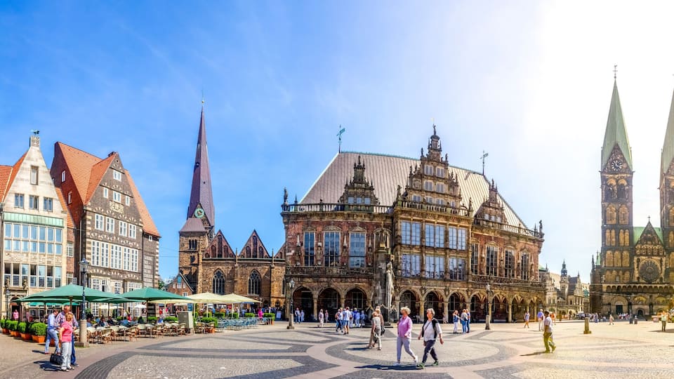 A historic square with cobblestone pavement, a prominent church with a tall spire, and a mix of traditional and modern buildings.