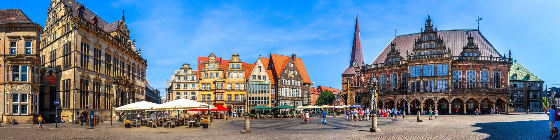 A historic European square with ornate buildings, a prominent church spire, and outdoor cafes.