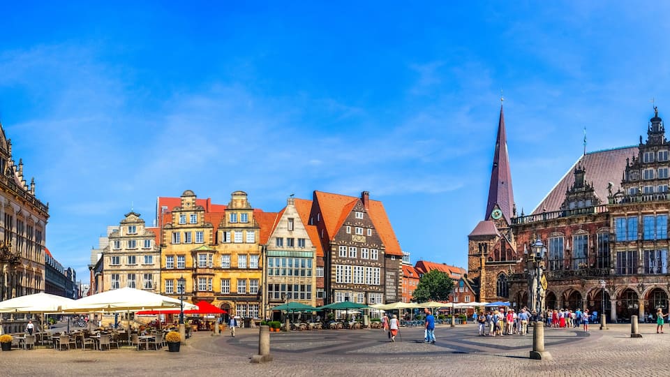 A historic European square with ornate buildings, a prominent church spire, and outdoor cafes.