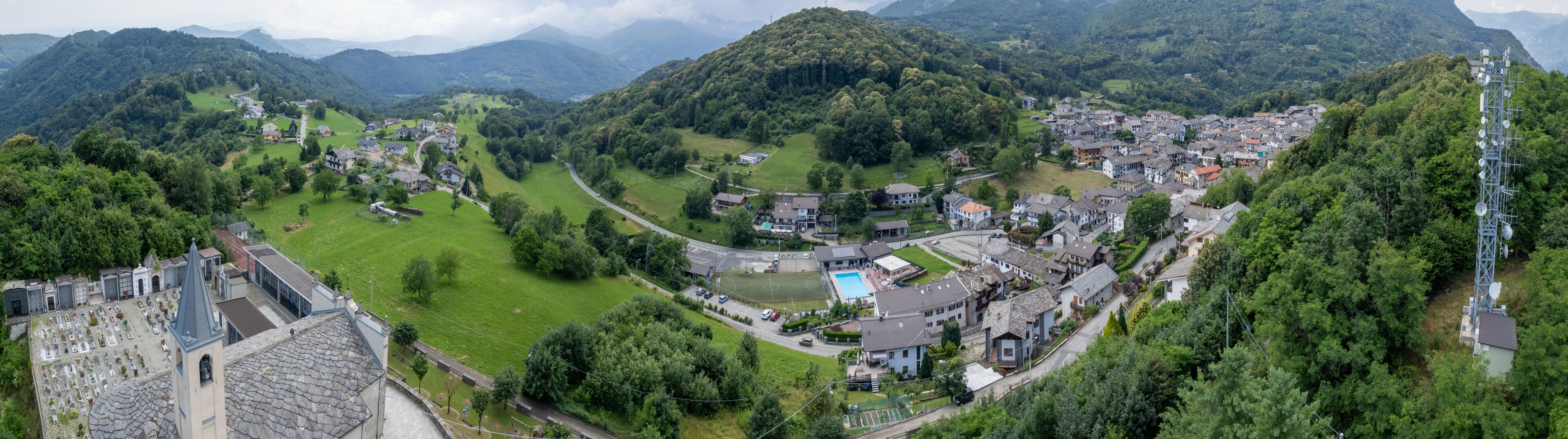 A town nestled in a valley surrounded by mountains, with a church, a cemetery, and a swimming pool.