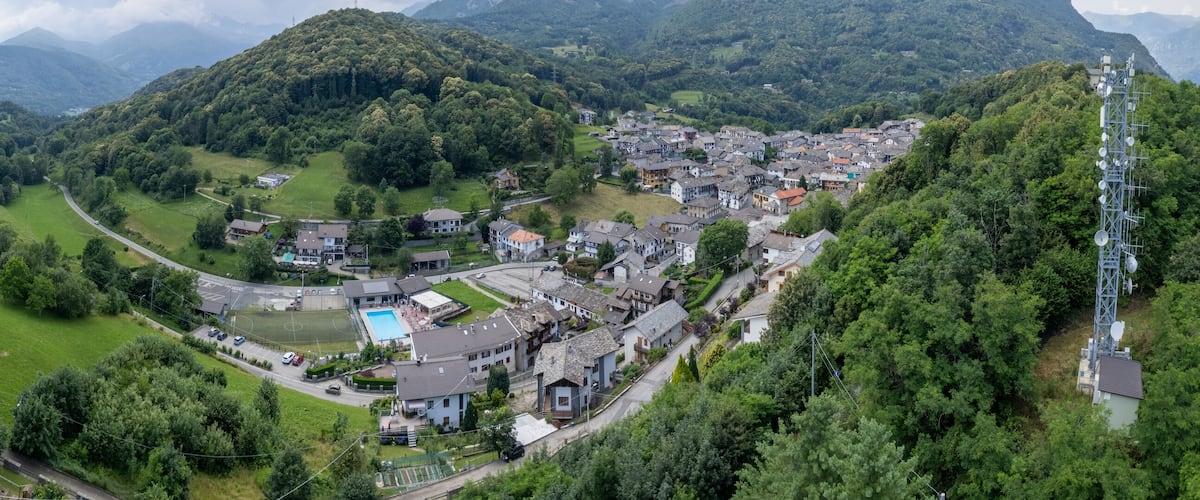 A town nestled in a valley surrounded by mountains, with a church, a cemetery, and a swimming pool.