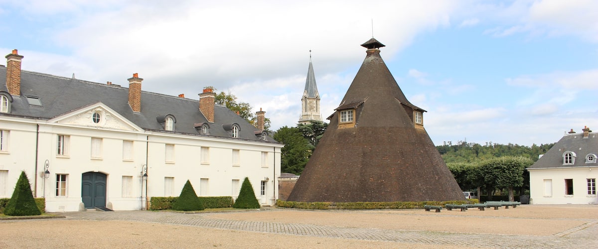 A historic building with a large conical roof, a church with a spire, and a cobblestone courtyard.