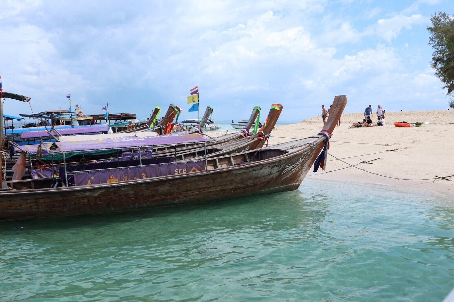 A traditional wooden boat docked at a beach with clear turquoise water.