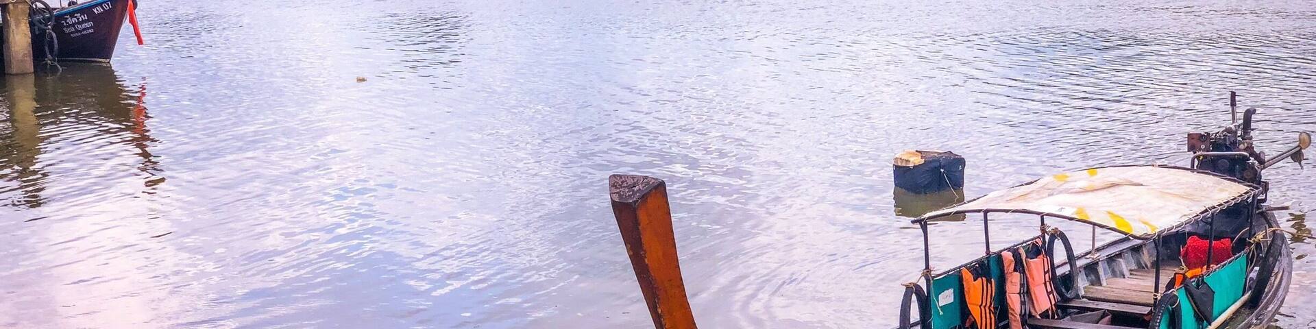 A calm lake with boats, a wooden dock, and a forested island in the background.
