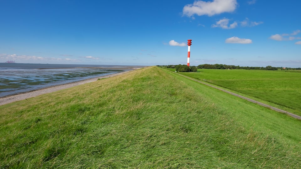 A grassy field with a red and white lighthouse on a hill by the sea.