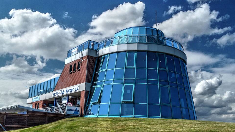 A modern building with a curved glass facade and a sign reading "Yacht Club Norden & W."