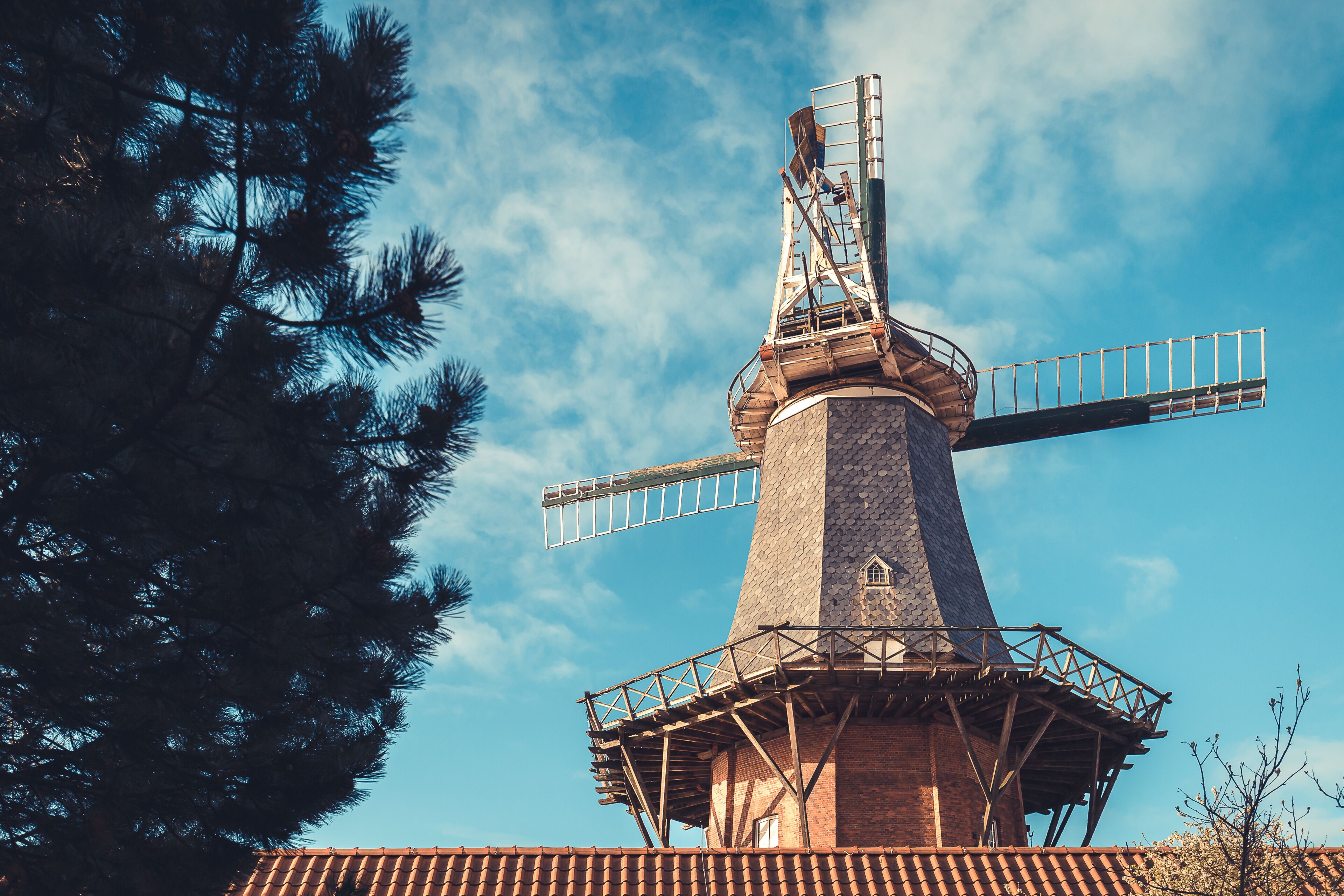A windmill with a brick base and metal framework, set against a clear blue sky.