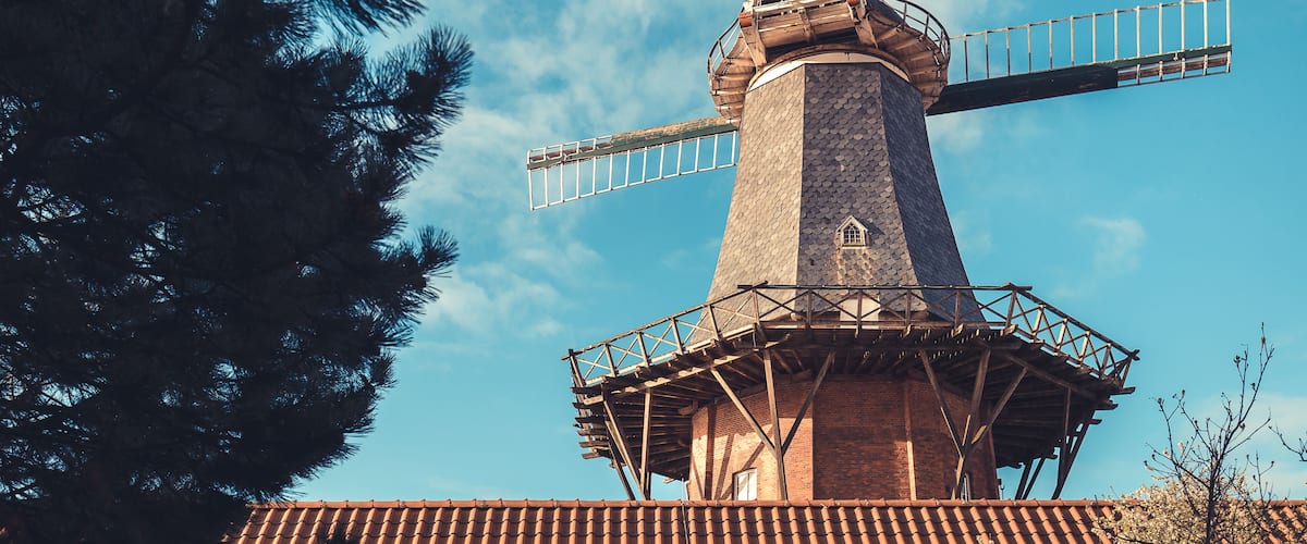 A windmill with a brick base and metal framework, set against a clear blue sky.