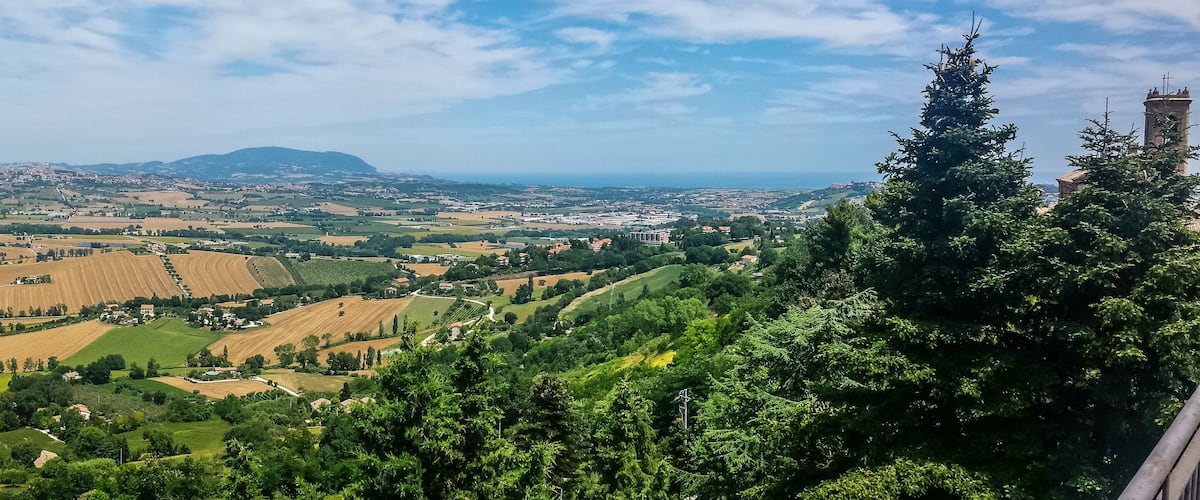 A panoramic view of a hilly landscape with fields, a distant mountain, and a tower.