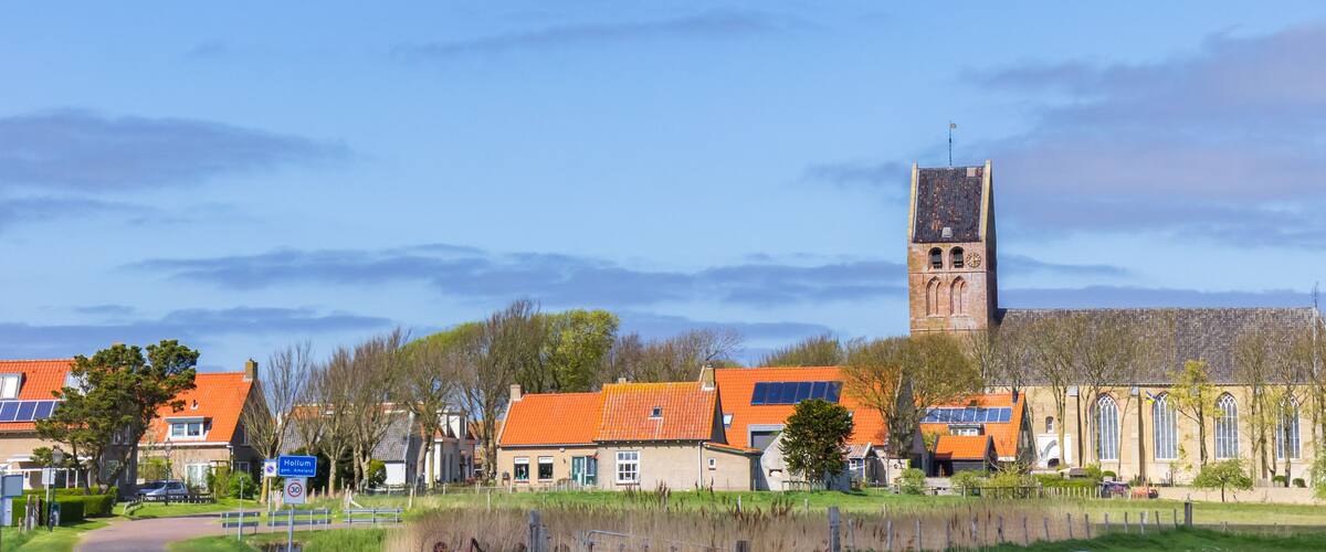 A town with a prominent church tower, orange-roofed houses, and a sign for 'Hollum.'